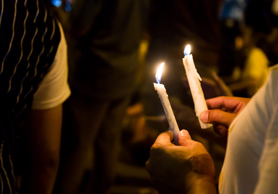 Group of people holding candle vigil in darkness seeking hope, worship, prayer